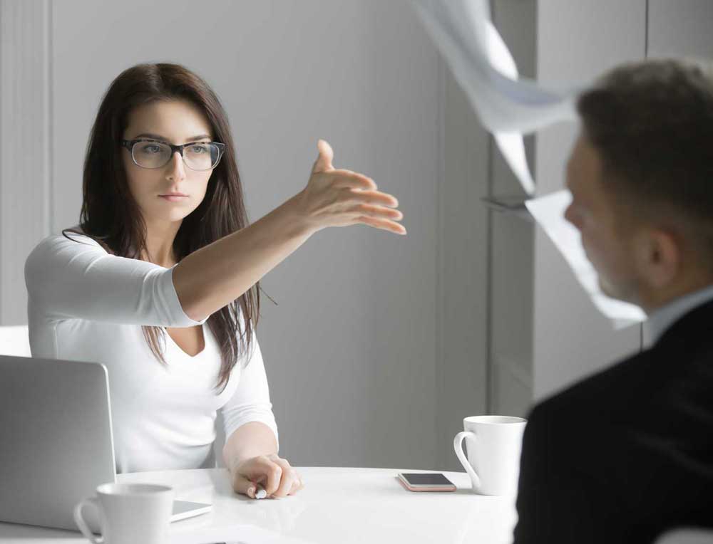 businesswoman aggressively gesturing to man across desk